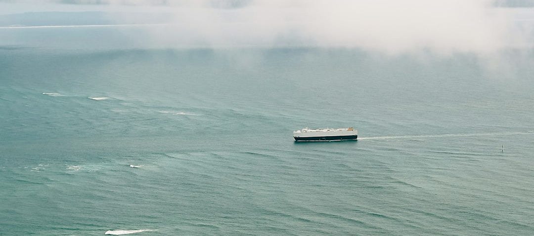 A lone cargo ship sails on a calm, green ocean.