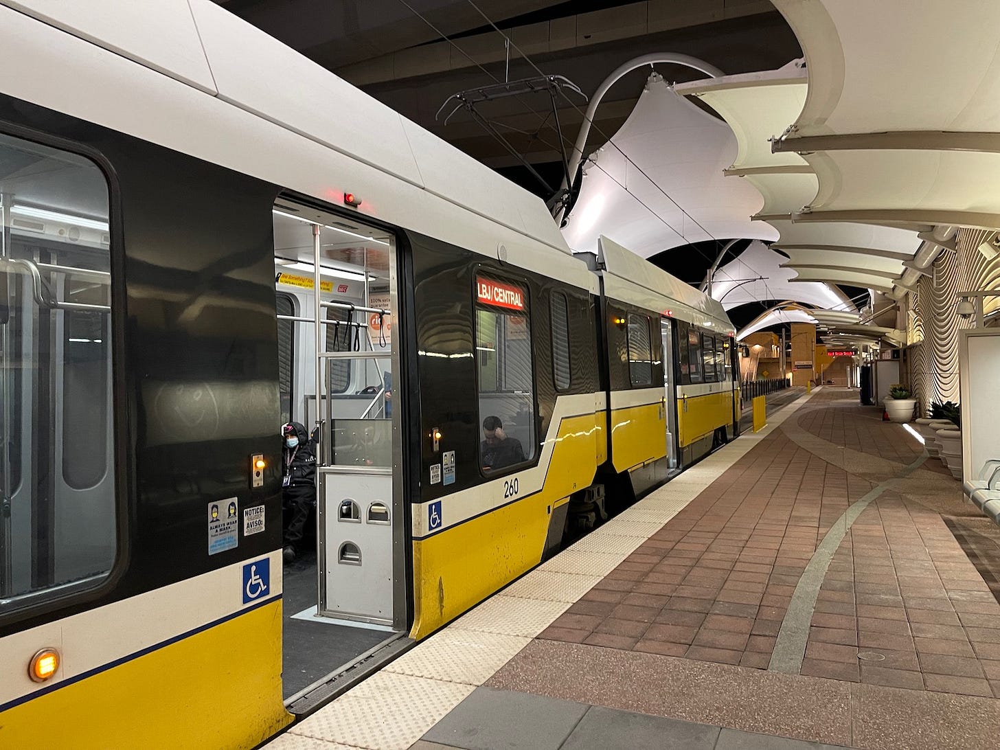 Dallas DART light rail train at LBJ/Central station, featuring accessible entry and modern architecture, highlighting public transit in the travel industry.