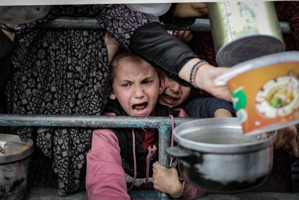 Palestinian children wait in line to receive food prepared by volunteers for Palestinian families ,displaced to Southern Gaza due to Israeli attacks,...