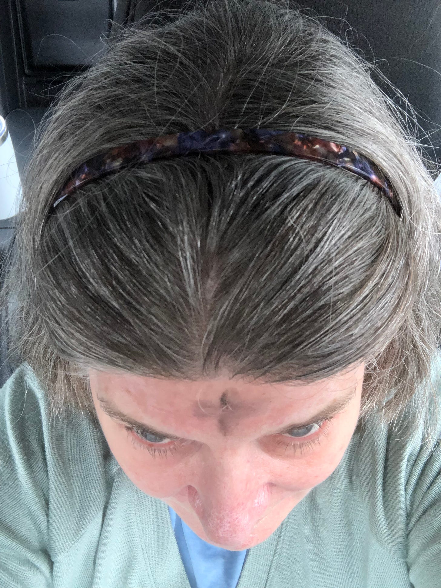 Looking down from teh top a woman’s head (graying hair, headband) to see a cross of ash on her forehead.