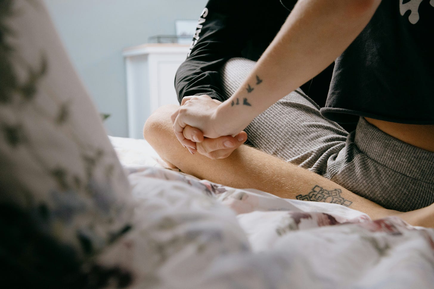 tattooed woman holding hands with man couple sitting on bed facing each other