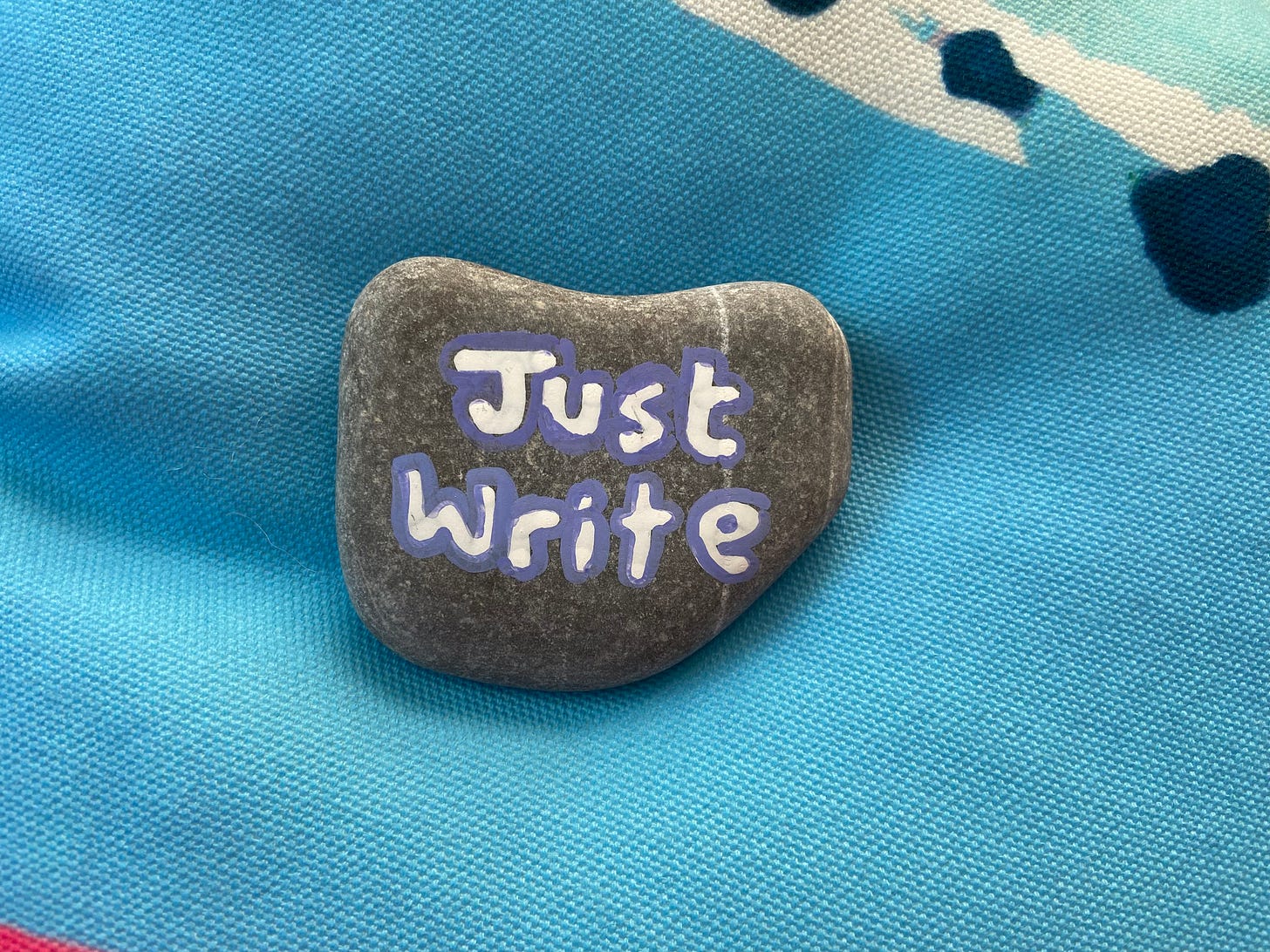 A rock with "Just write" painted on it, lying on a textured surface. A rock with "Just write" painted on it, lying on a textured surface.