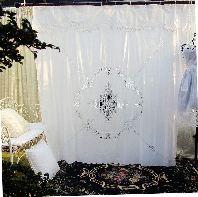 May include: White lace curtain with a large, intricate floral design in the center. The curtain is hanging from a metal rod and is in front of a white wall. The curtain is sheer and allows light to pass through it. The curtain is a beautiful and elegant addition to any home.