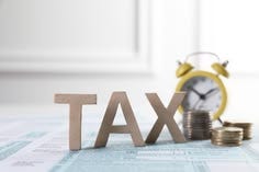 This may contain: a stack of coins next to an alarm clock with the word tax written on it This may contain: a stack of coins next to an alarm clock with the word tax written on it