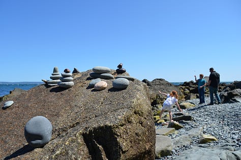 Lighthouse in Maine with rocky beaches and children playing.