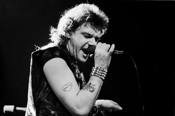 Paul Di’Anno, with tattoos on his arms and a leather vest, sings into a microphone.