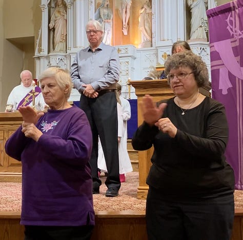Three photos are shown, are all of white individuals in a church sanctuary with a white altar and a large cross behind them. The first image at left shows a white woman in a navy blue dress with curly auburn hair. She is using sign language. She’s wearing glasses. In the next image a man with white hair and a light grey button-down dress shirt. He’s also speaking in sign language next to a woman at a podium making an announcement. She has long brown hair. Both are wearing glasses. At the right are two women singing in sign language, one on the left has short blond hair and is wearing a purple sweatshirt, the other is wearing a dark colored dress and has curly brown hair. 