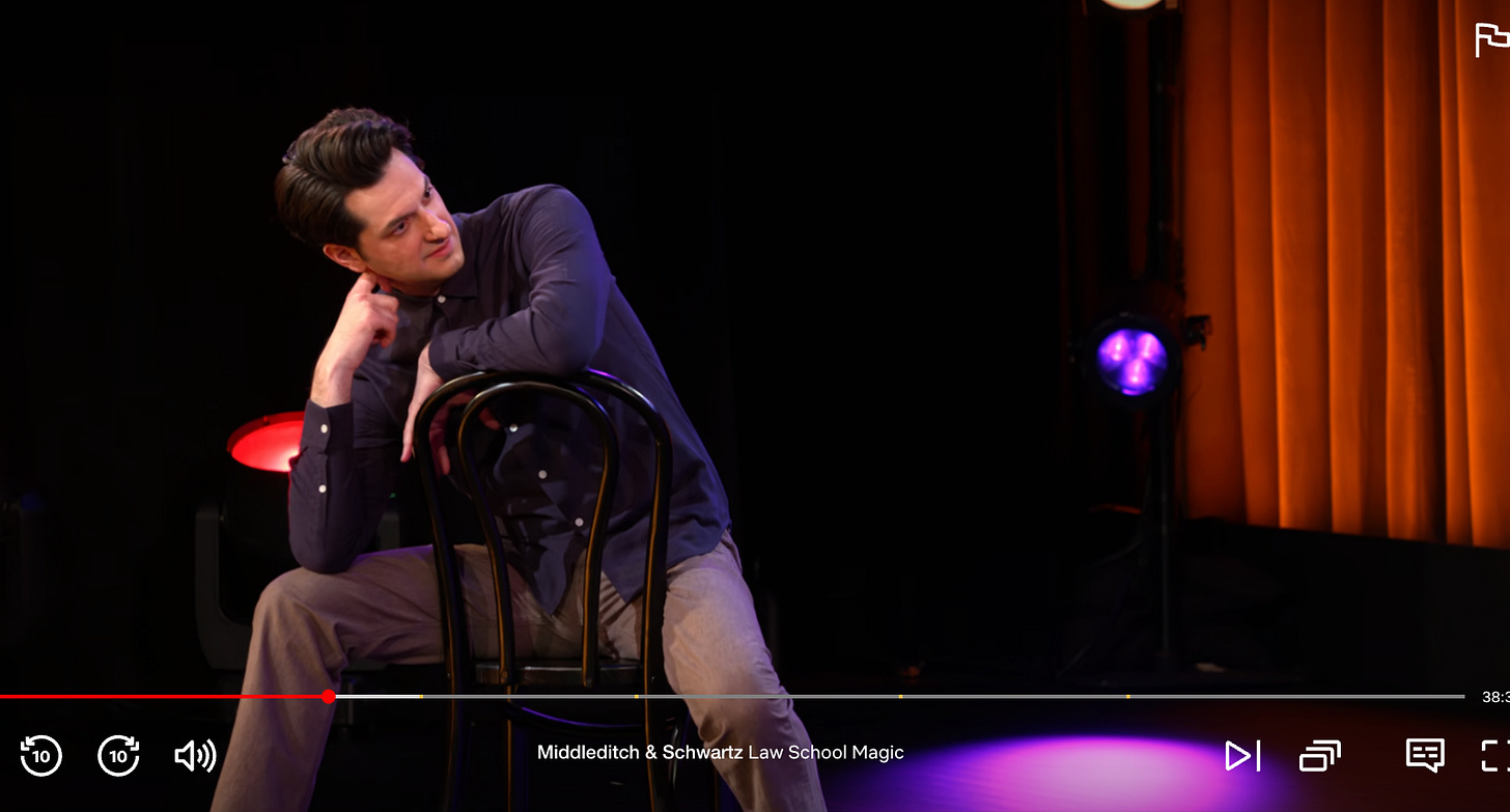 a screenshot of ben schwartz leaning back in a chair that's facing the wrong way