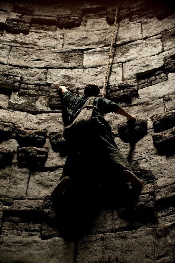 This may contain: a man climbing up the side of a stone wall with ropes hanging from it's sides