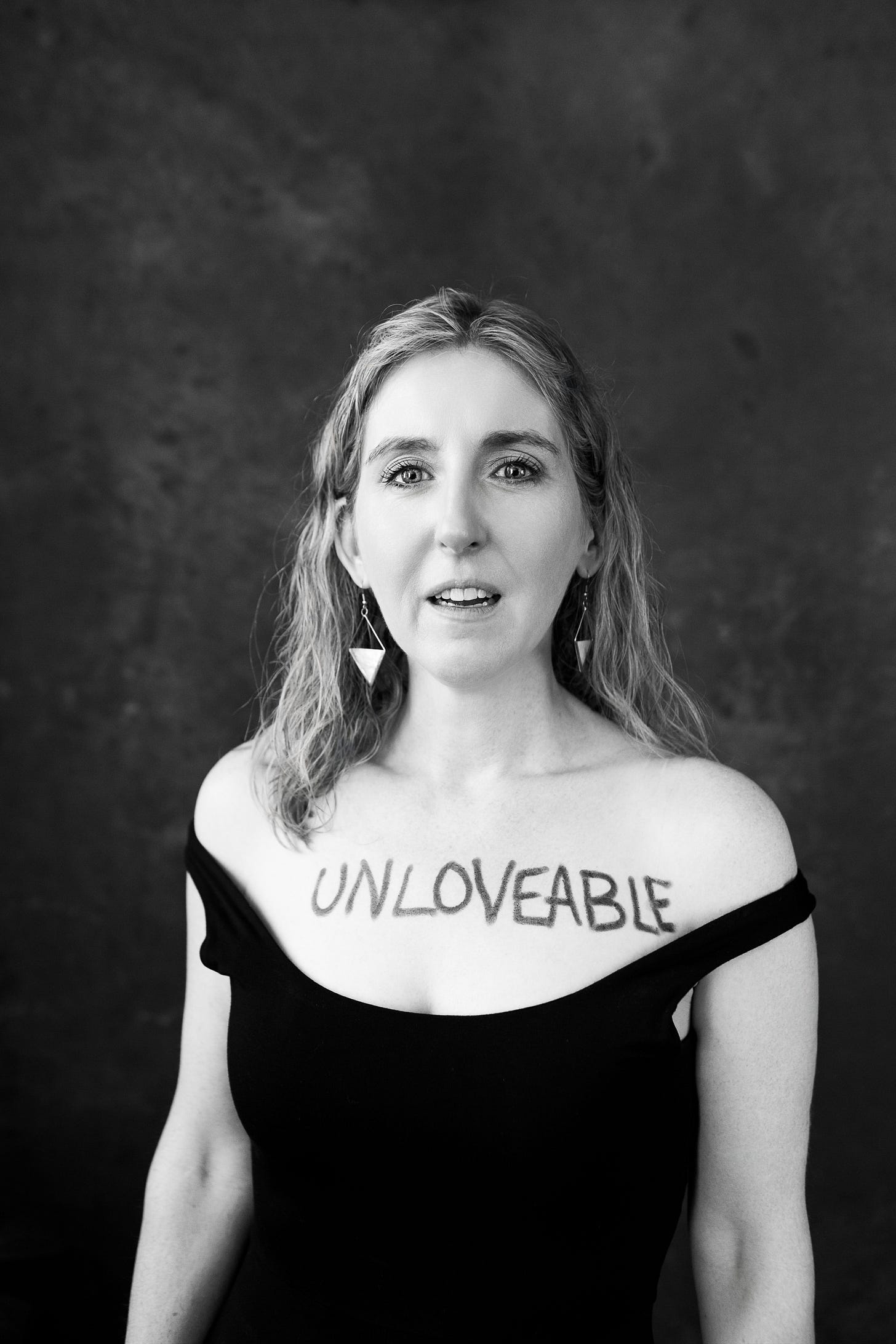 Black and White photo of a woman with the word unloveable written on her chest