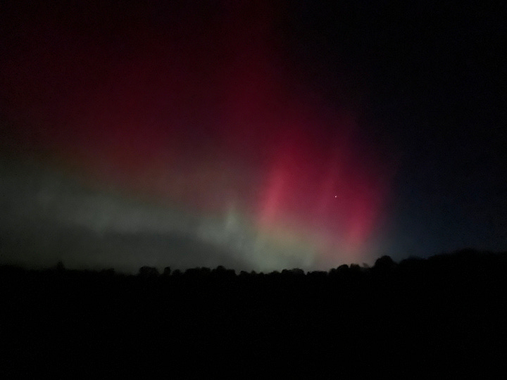 Pink and green lights over a black landscape.