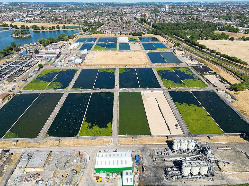 industrial facilities in the foreground, filter beds in blue and green in the middle, London stretching into the distance behind them