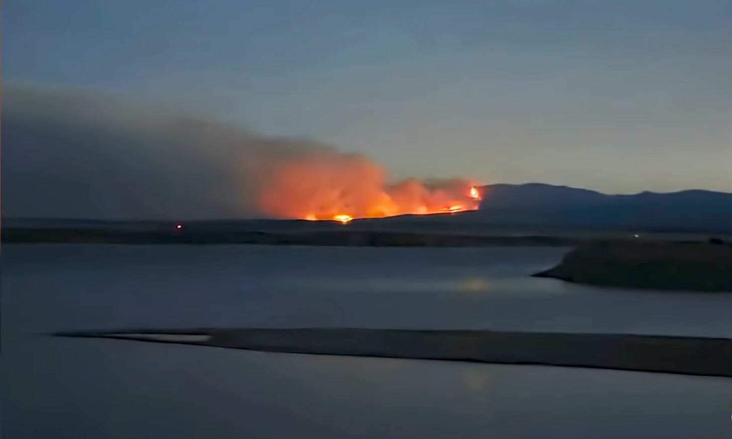Dusk or dawn, fire blazes orange across a lake.