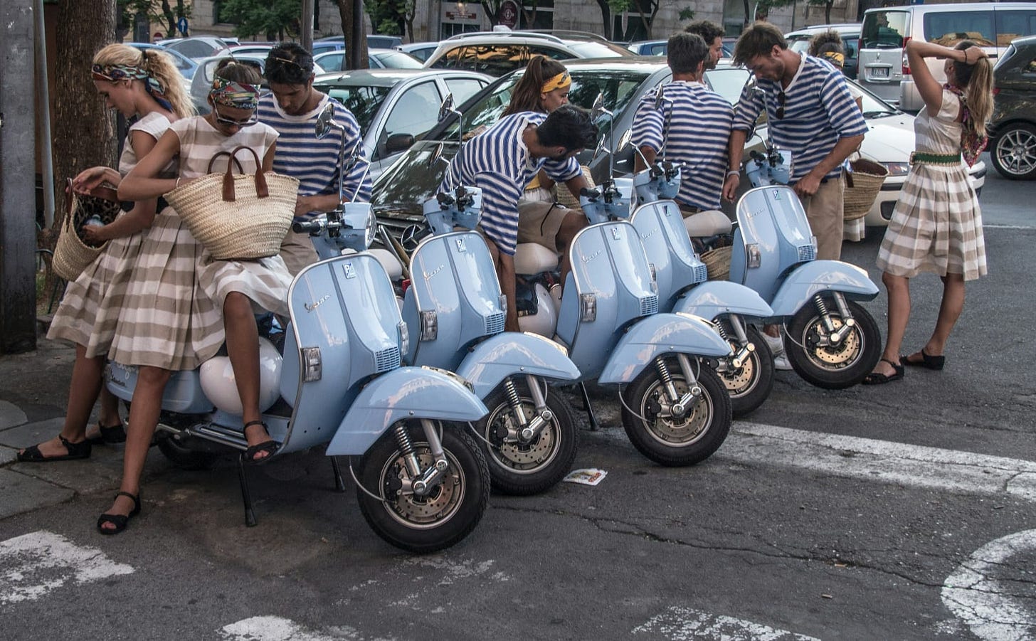 a row of blue vespas with attractive women and men in striped outfits sitting on them