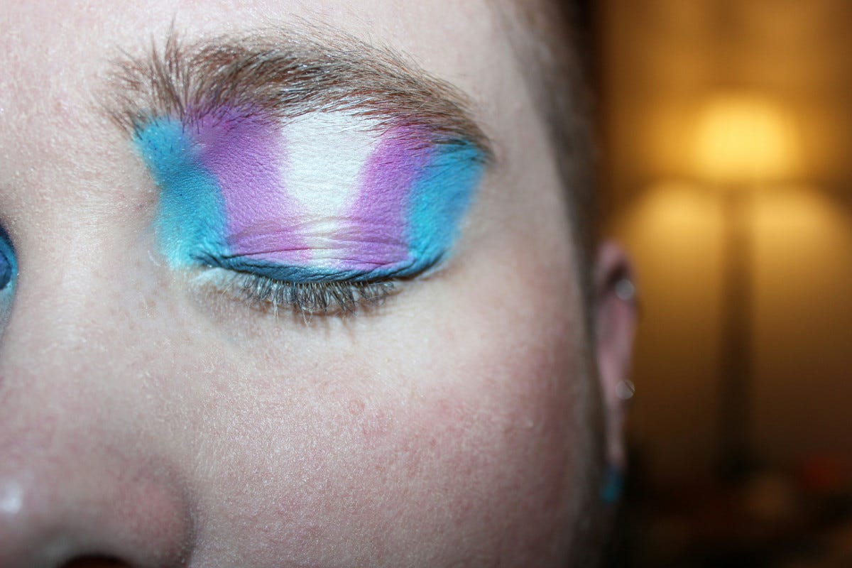 Closeup of a person’s face with an eyelid painted in the colors of the pro-trans movement. Closeup of a person’s face with an eyelid painted in the colors of the pro-trans movement.