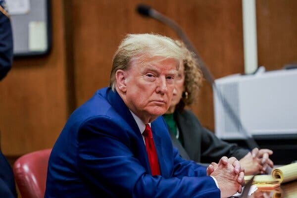Donald Trump in a blue suit and red tie, sitting at a table.