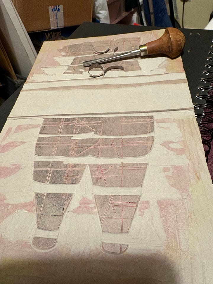 on the left, a grey block with the bottle shaped kilns and their reflections, half carved as I despaired about the mistake, and on the right me continuing to carve it a week later - one of the cutters is lying n the block, with some curls of lino as evidence of activity.