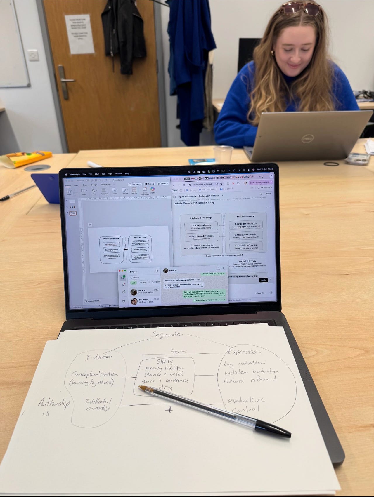 A laptop open to PowerPoint and Claude sits on a meeting table beside a sheet of paper covered in handwritten notes and arrows, with a pen resting across the page. In the background, a colleague works quietly on her own laptop. WhatsApp conversations with two trusted collaborators are part of the unseen workflow behind the scene: a moment of intense ADHD-fuelled hyperfocus, trying to translate a complex idea into something other people could finally understand.