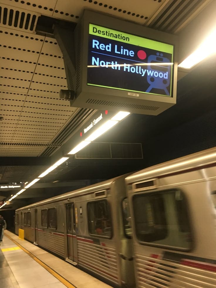 This may contain: a silver train traveling past a station next to a sign that says red line north hollywood