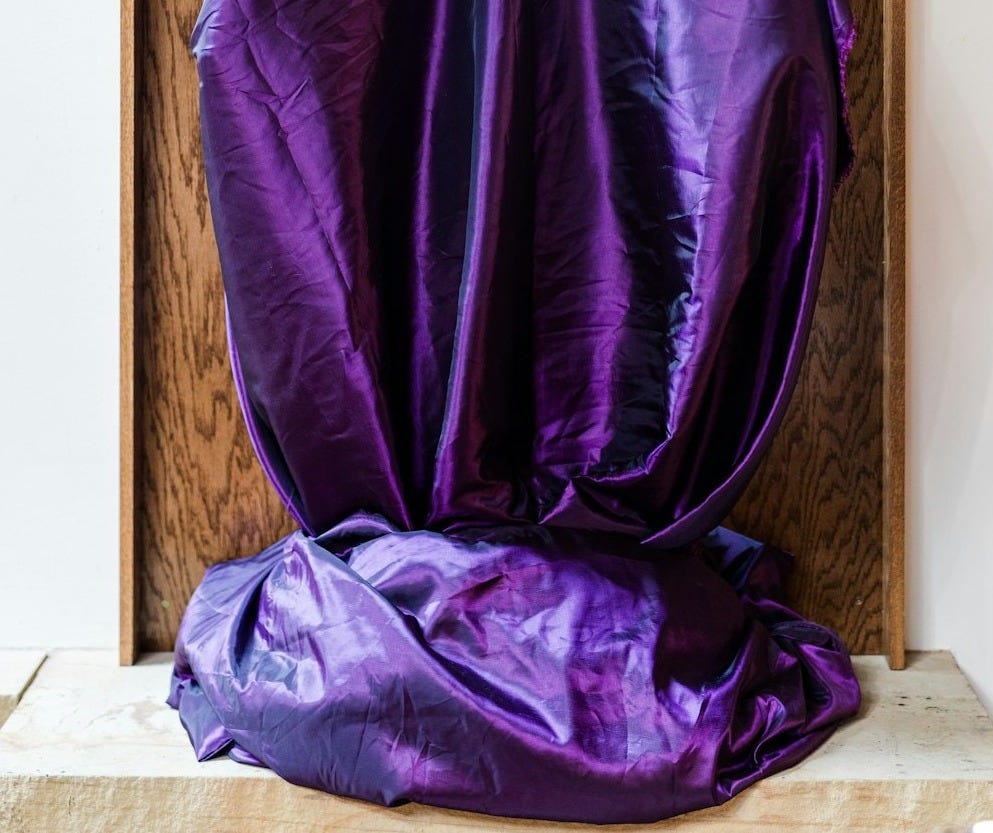 A veiled figure draped in purple fabric stands. A veiled figure draped in purple fabric stands.