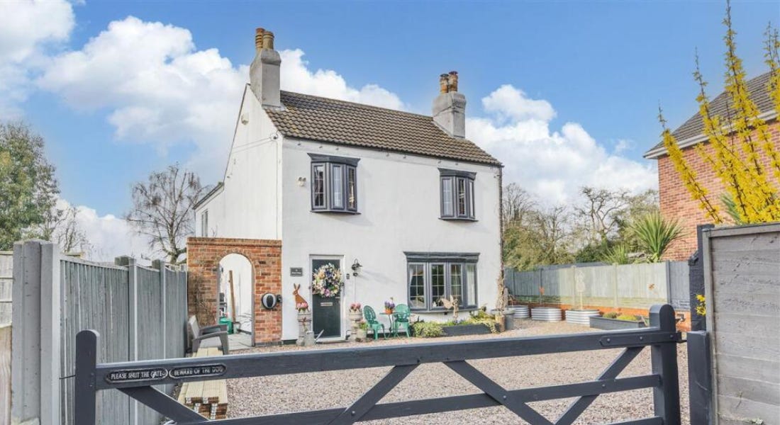 A white house with a brick archway to the left, a gravel driveway, and a black fence door A white house with a brick archway to the left, a gravel driveway, and a black fence door