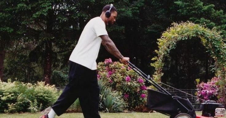 This may contain: a man pushing a lawn mower in the yard