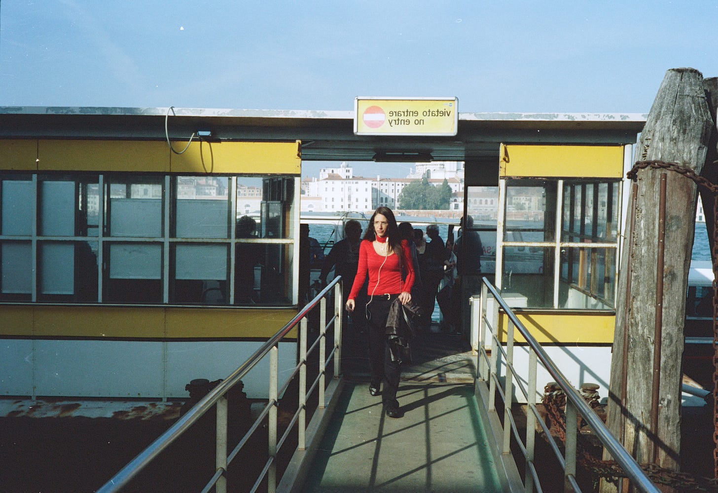 A woman in a red top and black trousers walks off a vaperato water bus in Venice.