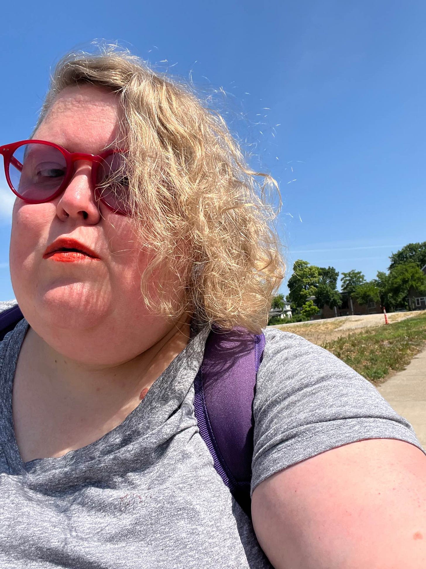 Me, Alison, a fat, white woman with asymmetrical curly blonde hair that in front of blue sky and trees in the distance