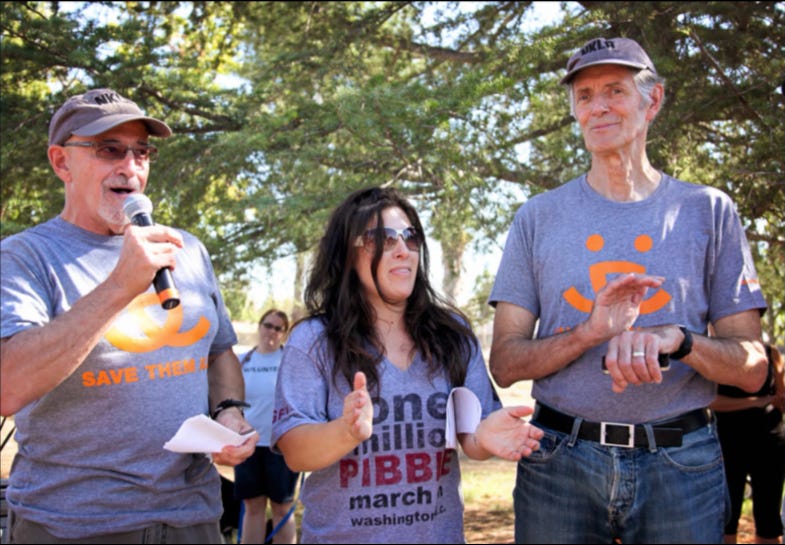 Rebecca Corry stands between Best Friends Animal Society co-founders Francis Battista, left, and Gregory Castle, right, at an outdoor event; both men wear gray Best Friends shirts.