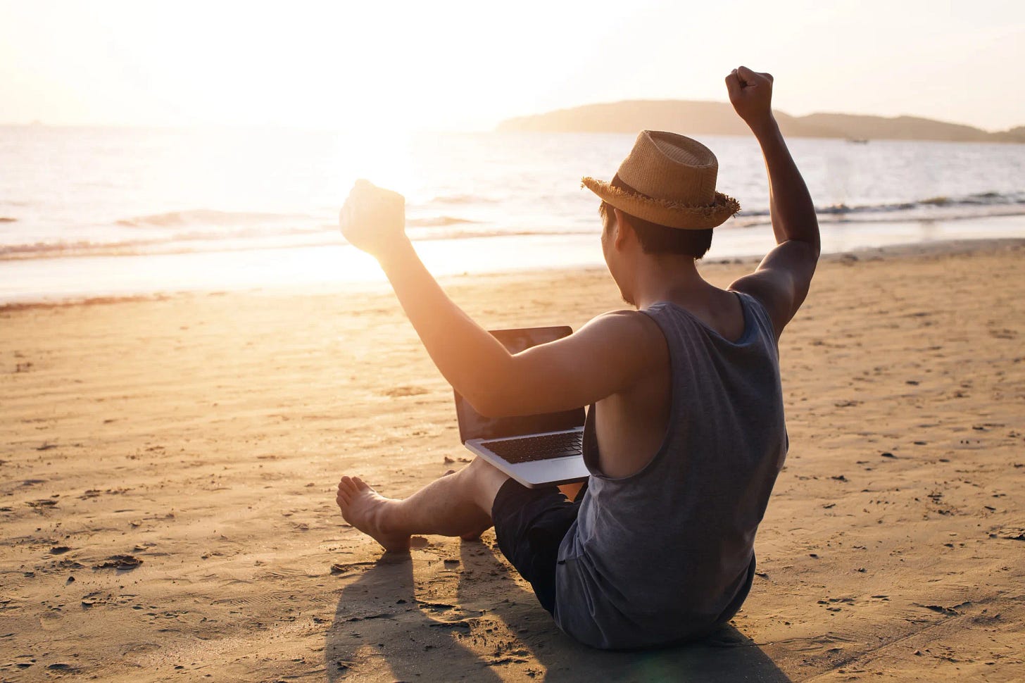Hombre sentado en la playa celebrando que puede dejar de trabajar el resto de su vida