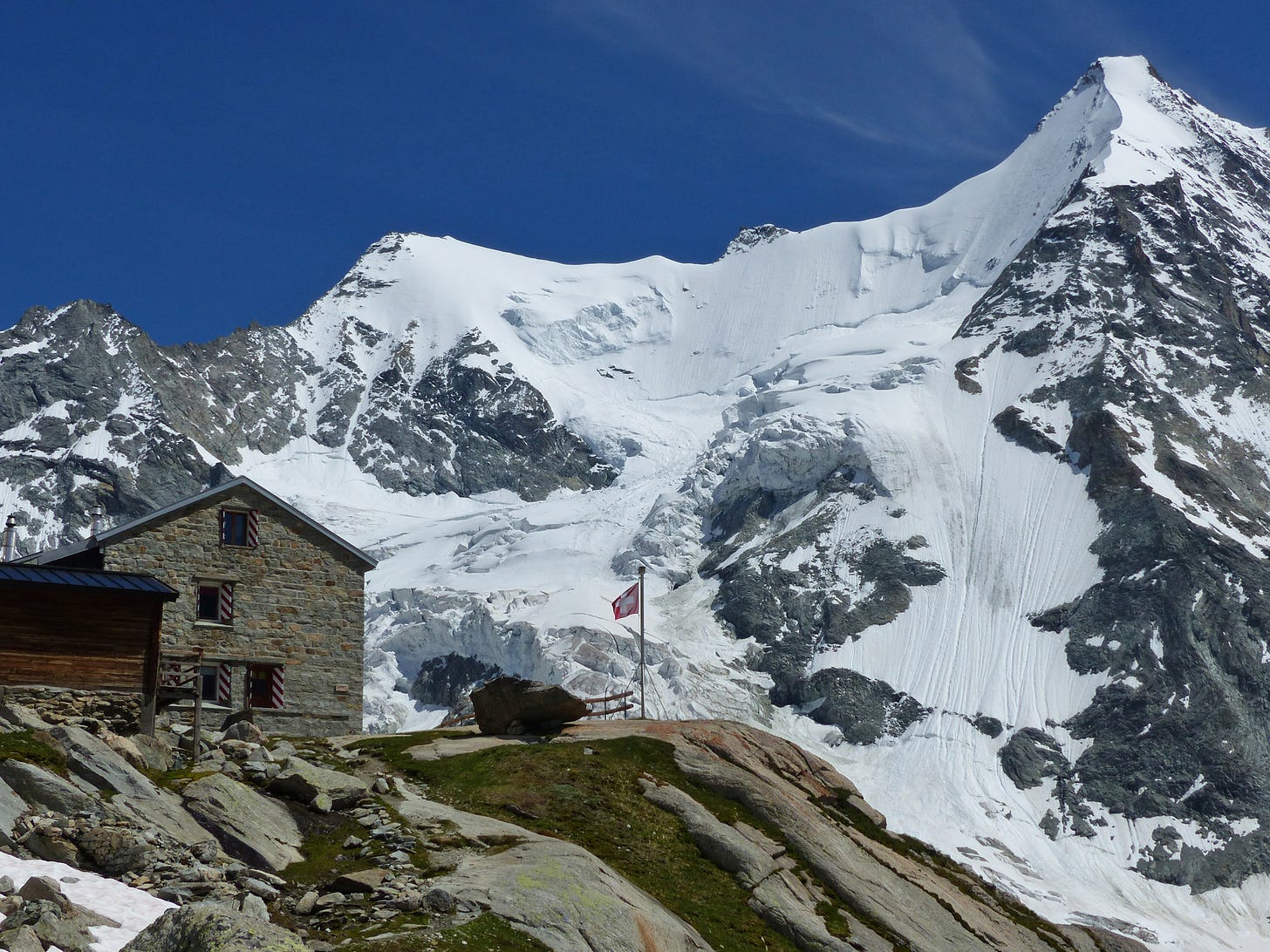 Mountain ice and rock, stone-built mountain hut in foreground, Swiss flag flying