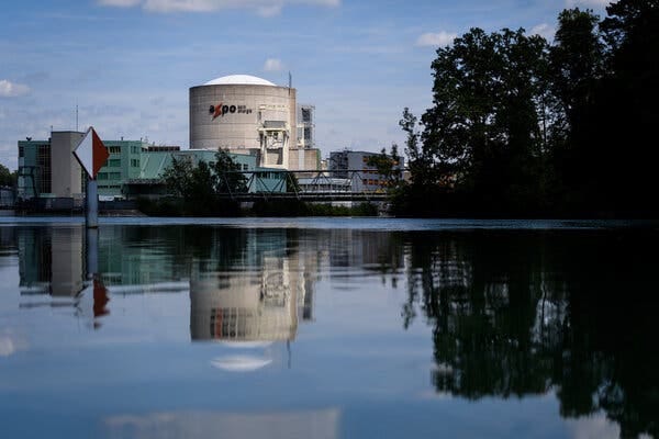 A view of a silo with a white top seen from across a lake with trees to the right. 