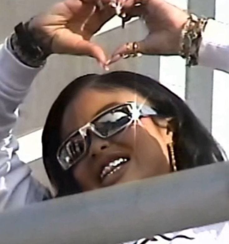 This may contain: a woman wearing sunglasses and holding her hands up to her face