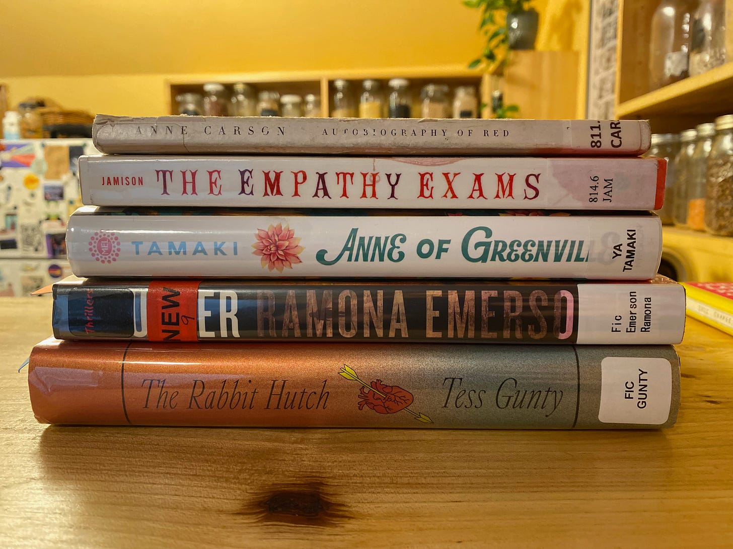 The five listed books stacked on a wooden counter with kitchen shelves and a fridge visible in the background.