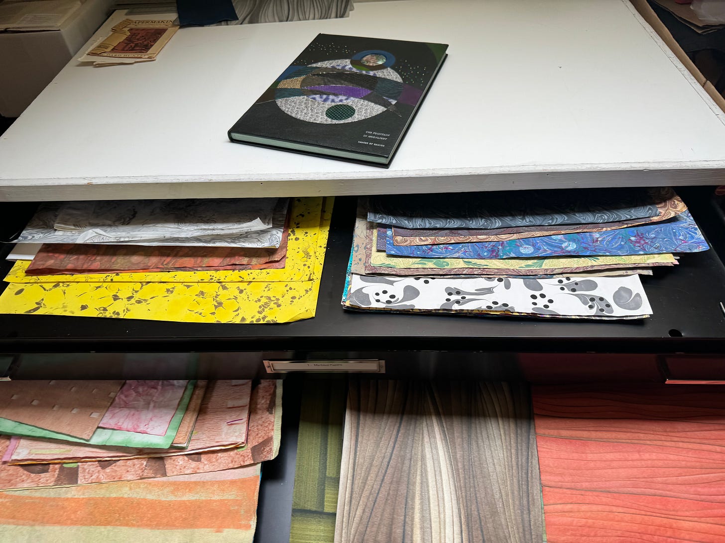 A few layers of drawers filled with decorative papers that have all kinds of colors and textures.