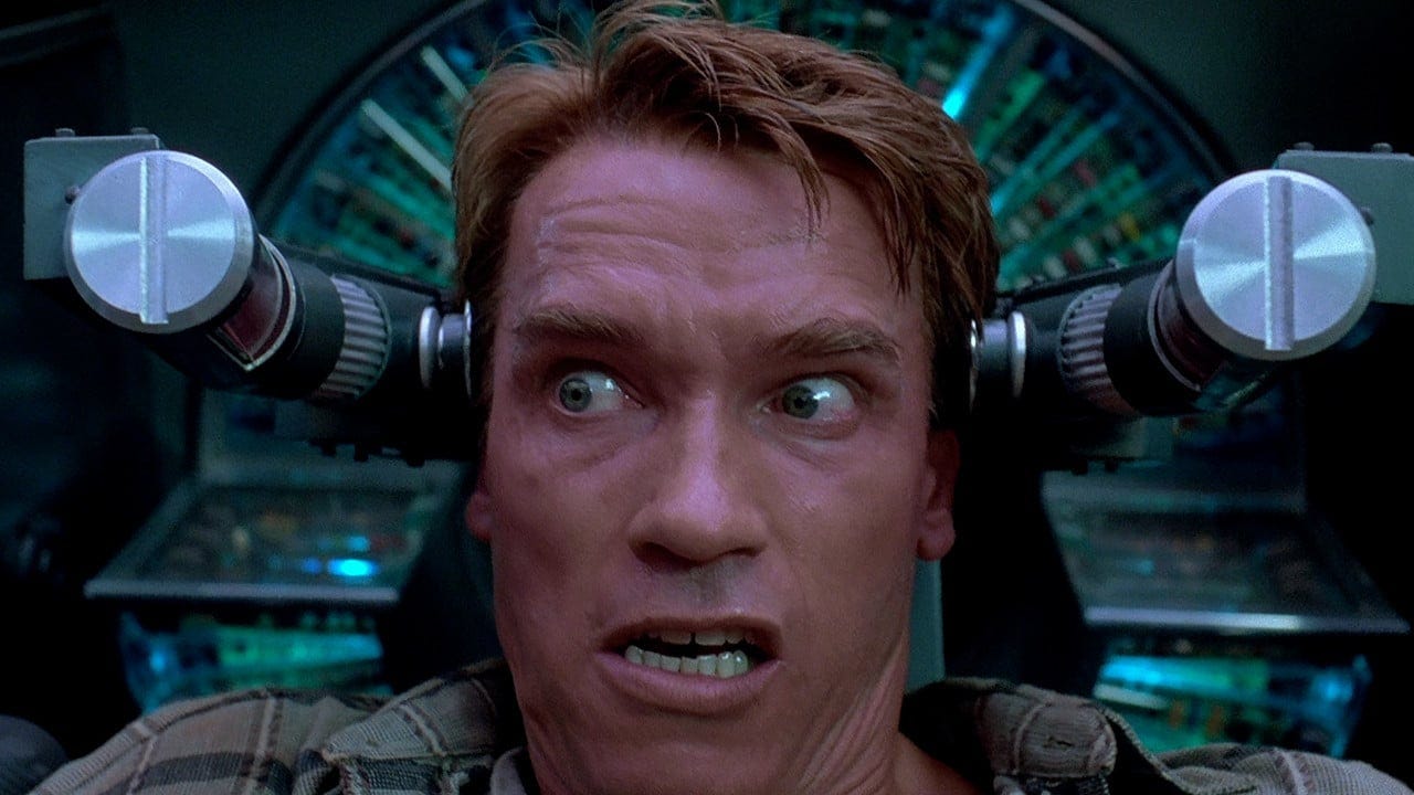 Screenshot from Total Recall with Arnold Schwarzenegger making a scared face, with weird machinery either side of his head.