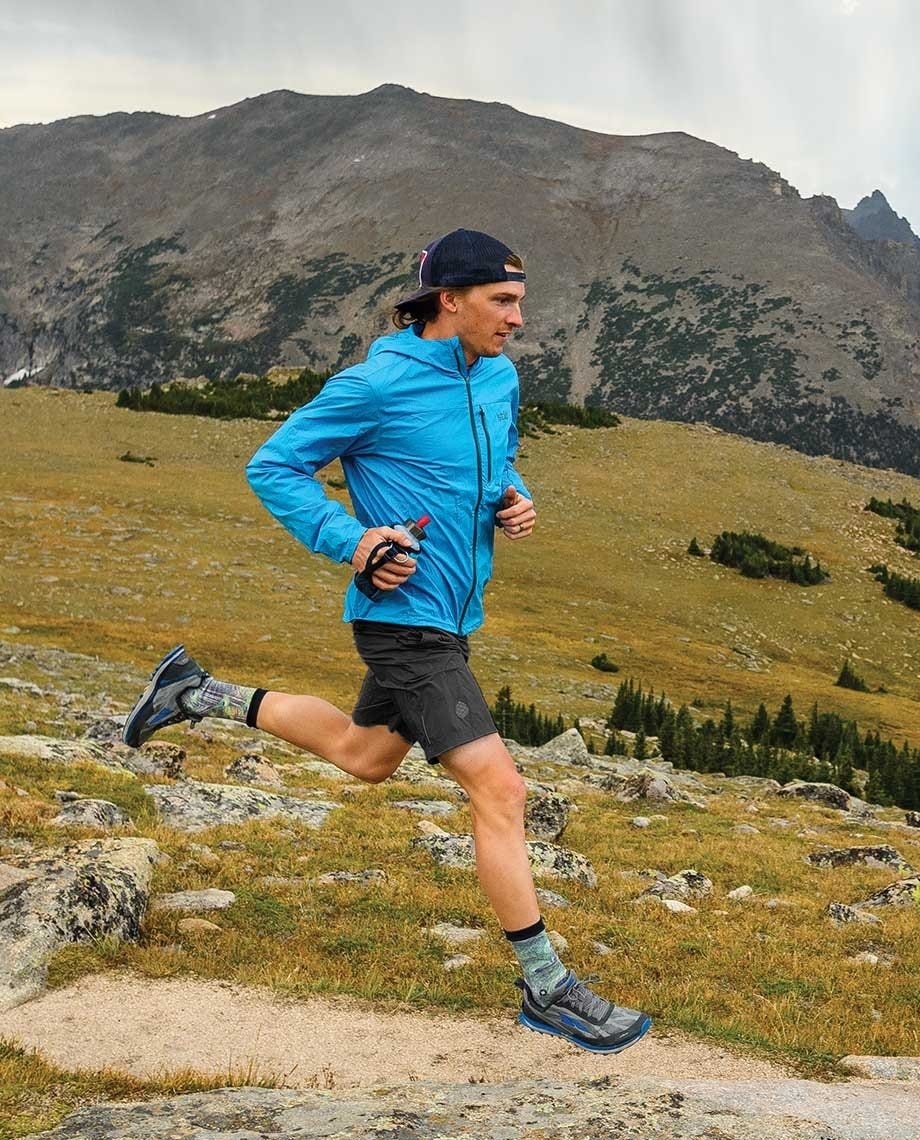 a man runs wearing the stio second light windshell