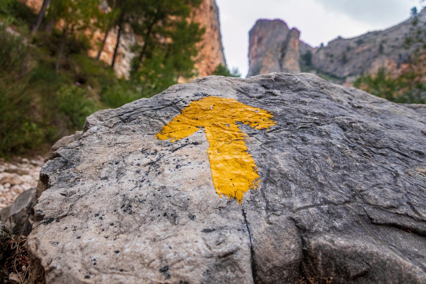 A yellow arrow painted on a rock along a rugged path, representing guidance and recalibration.