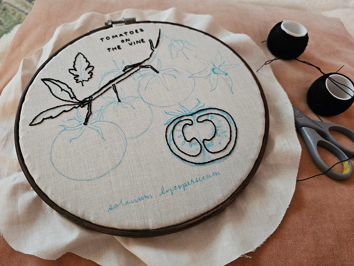 on the left (or top) is a stack of embroidery hoops set with fabric, at the right (or bottom) is an in-progress embroidery with spools of thread set on a pink pillow
