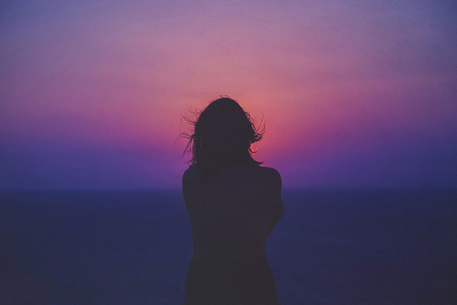 Silhouette of a woman against a dark pink, purple dusk sky and sea. Silhouette of a woman against a dark pink, purple dusk sky and sea.