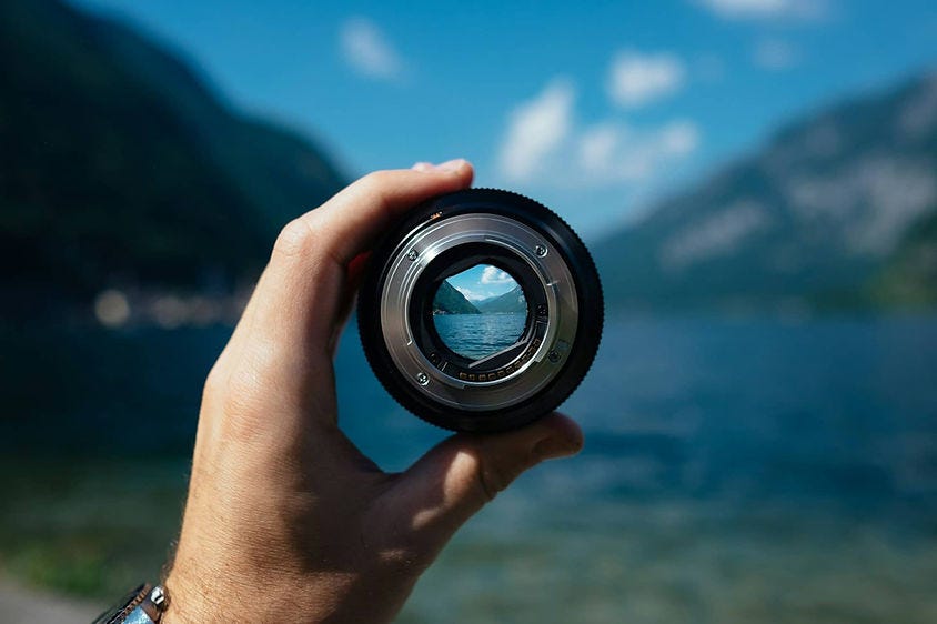 Hand holding a camera lens looking at a mountain view.