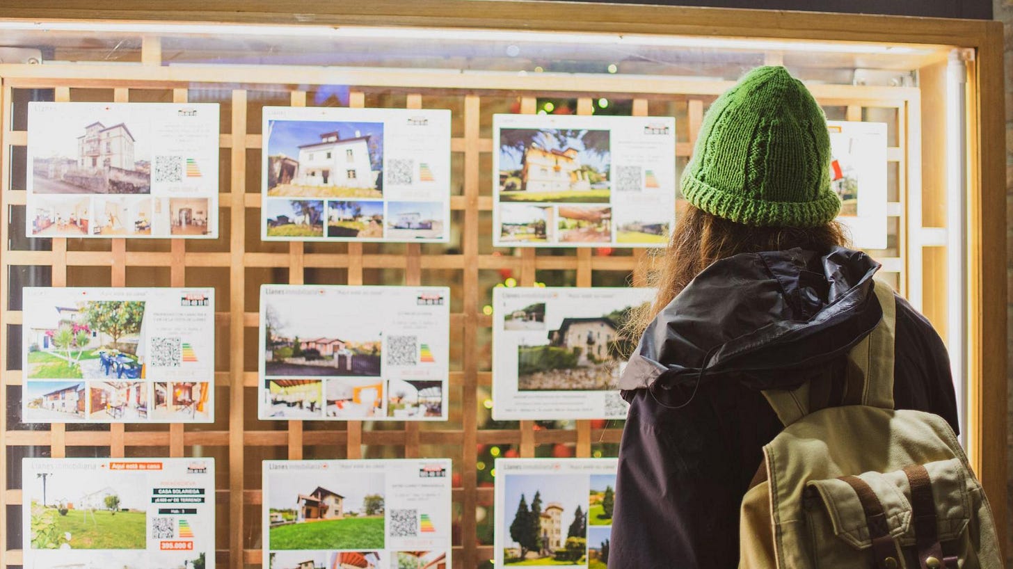 Woman wearing a green beanie hat looks at house prices in a store window Woman wearing a green beanie hat looks at house prices in a store window