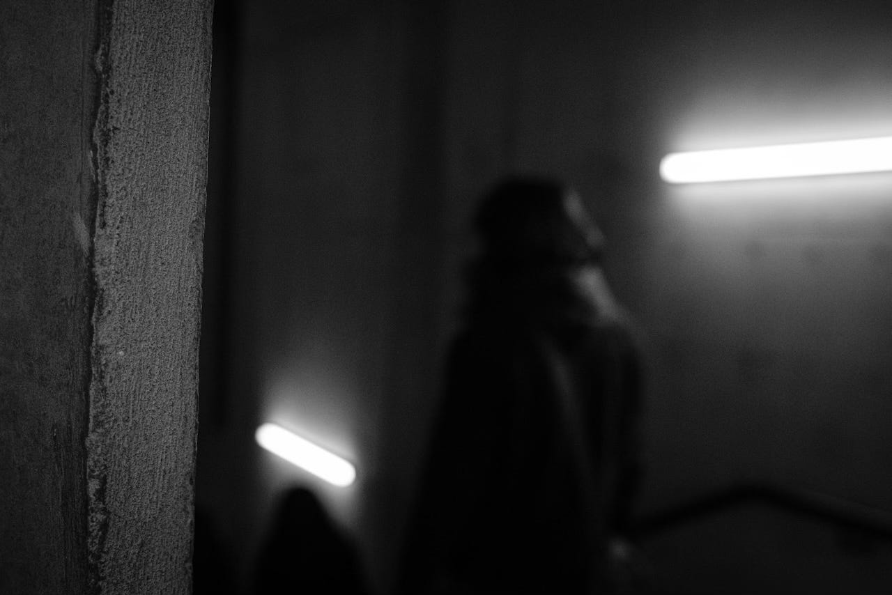 a black and white, low-light image of blurry silhouettes walking down stairs in a huge concrete building.
