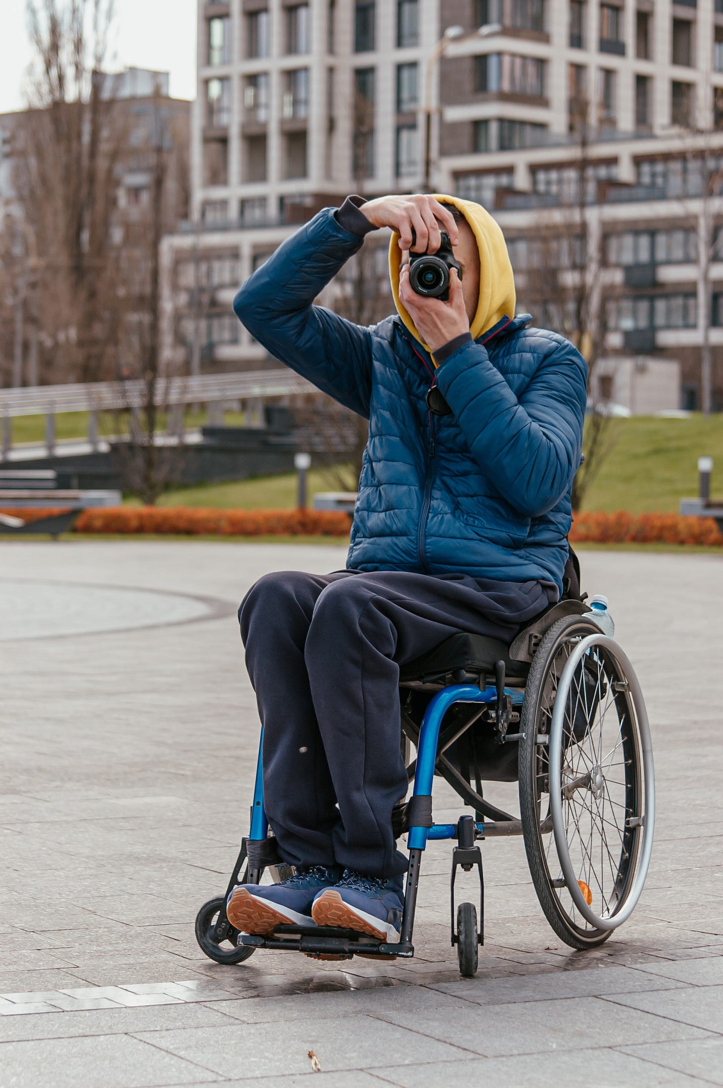 Wheelchair user takes a photo, he wears a yellow hoodie and a blue jacket.