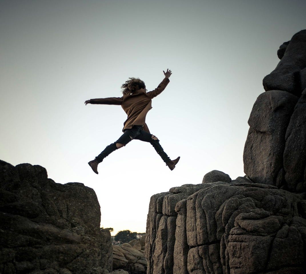 person jumping on big rock under gray and white sky during daytime person jumping on big rock under gray and white sky during daytime