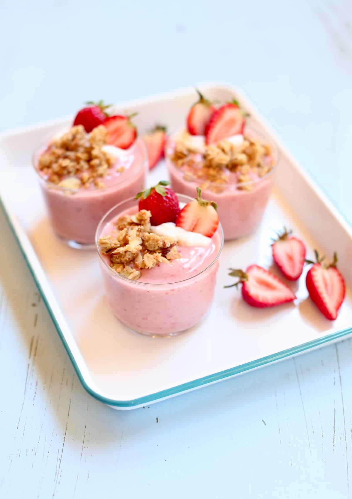 a whote tray holding several strawberry smoothies with fresh strawberry garnish on the side.