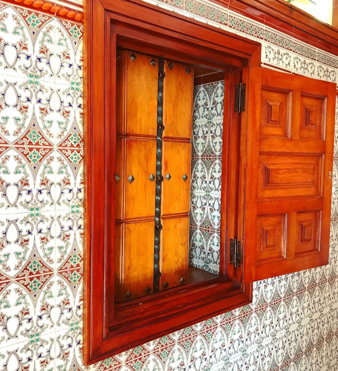 una finestrella di legno su una parete di maioliche bianche, rosse e blu