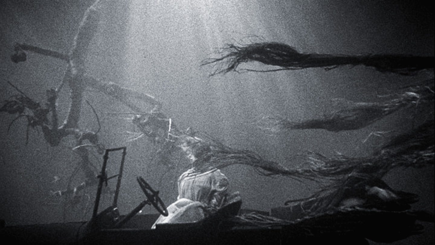 Underwater shot of a woman’s lifeless body seated upright in a submerged car, her hair drifting with the current as light pierces down from above. Underwater shot of a woman’s lifeless body seated upright in a submerged car, her hair drifting with the current as light pierces down from above.