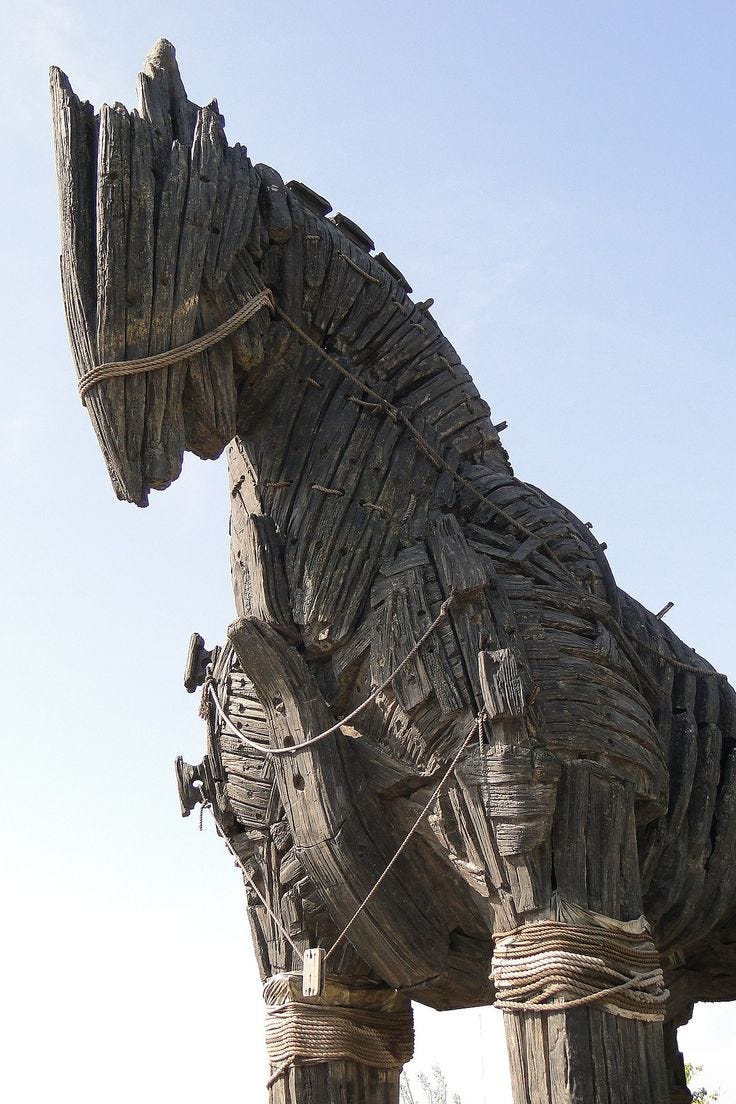 This may contain: a large wooden horse statue sitting on top of a lush green field under a blue sky