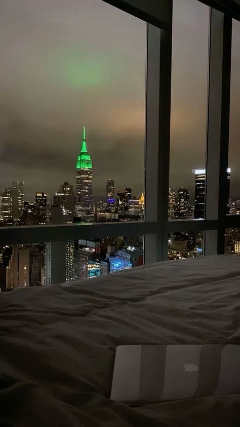 This may contain: a bed in a room with a view of the city at night and green lights